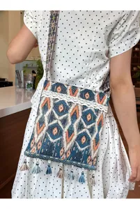Bolso cruzado de estilo étnico con patrones geométricos, encaje decorativo y borlas coloridas.