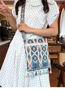 Vista detallada de bolso cruzado étnico con patrones geométricos ikat, encaje y borlas.