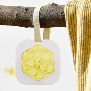 Close-up van een decoratief hangend geurtablet met geel bloemenreliëf en een beige lint.