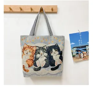 Canvas tote bag featuring a cute three-cat woven tapestry pattern and striped handles.