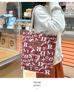 Detailansicht der burgunderroten Segeltuchtasche mit weißem Buchstabenprint und Kordel.