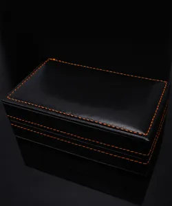 Coffret cadeau en cuir noir avec surpiqûres orange, emballage professionnel pour accessoires chic.
