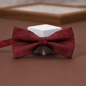 Detail shot of the wine red patterned bow tie, showing fine fabric texture and classic leaf design.
