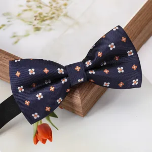 Gros plan d'un nœud papillon bleu foncé avec motif floral blanc et orange pour costume.