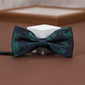 Close up of a dark blue retro floral jacquard bow tie with green patterns on a brown display.
