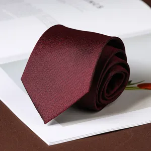 Detailed view of a burgundy textured necktie rolled neatly on a white book for business wear.