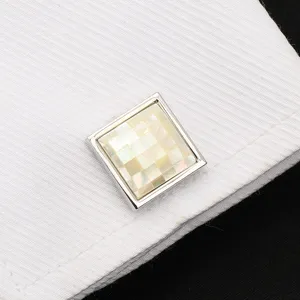 Gros plan de manchette carrée en nacre avec motif à carreaux sur poignet de chemise blanche.