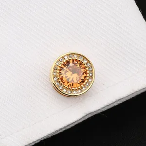 Détail en gros plan d'un bouton de manchette rond doré avec cristal ambre et strass.