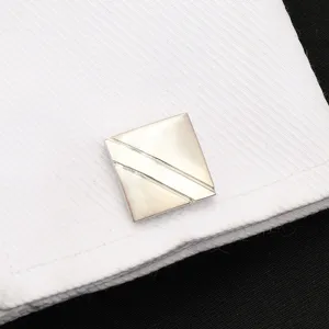 Gros plan détaillé de boutons de manchette géométriques argentés sur chemise blanche.