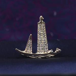 Close-up of the gold rhinestone sailboat brooch, showing sparkling crystal details.