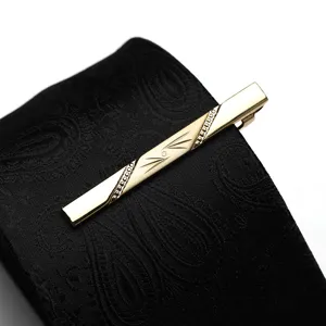 Close-up of a gold metal tie clip with delicate engraved details clipped on a black patterned tie.