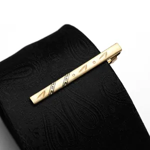 Gold metal tie clip detail showing leaf engravings and polished surface on black patterned necktie.
