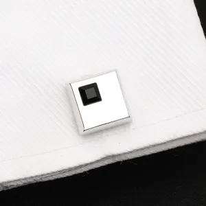 Gros plan sur un bouton de manchette carré argenté avec un cristal noir sur une manchette blanche.