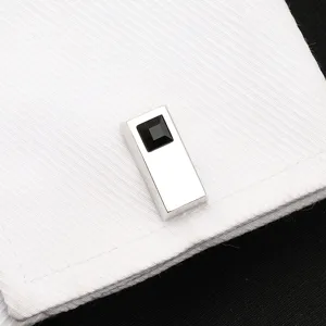 Gros plan d'un bouton de manchette argenté avec cristal noir sur une manchette de chemise blanche.