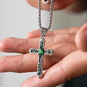Detailed closeup of retro cross pendant necklace with green stones and vintage silver chain.