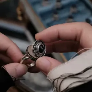 Primo piano dettaglio di un anello medaglione argento vintage con scatola apribile e pietra nera.