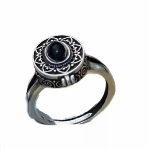 Primo piano di anello medaglione vintage in argento con pietra nera e motivi retrò.