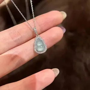Close-up detail shot of a sparkling diamond-paved green gourd pendant necklace on hand.