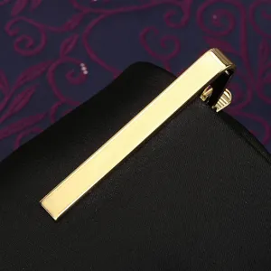 Golden metal tie clip detail view, minimalist long bar design for mens formal business wear.