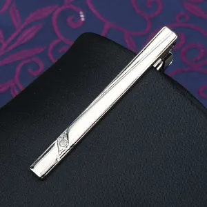 Close-up of a stylish silver metal tie clip featuring elegant engraved patterns and stone.
