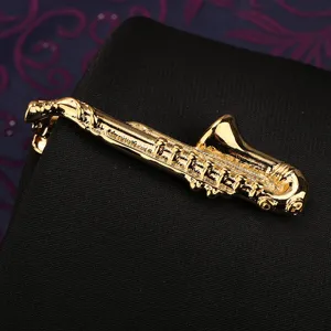 Dettaglio pinza cravatta sassofono dorata con finitura in metallo lucido e forma di strumento musicale.