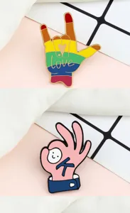 Close-up detail of cute cartoon hand gesture enamel pins featuring rainbow love and pink OK designs.