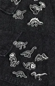 Detailed shot of black and white alloy dinosaur skeleton brooches displayed on dark denim fabric.