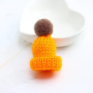 Mini knitted hat brooch detail shot, cute orange yarn beanie with brown pompom charm for decor.