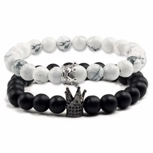 Dettaglio ravvicinato del set di bracciali di perle con ciondoli a corona, pietre nere e bianche.