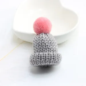 Close-up detail of cute grey knitted mini hat brooch with pink pom-pom pendant for bag decoration
