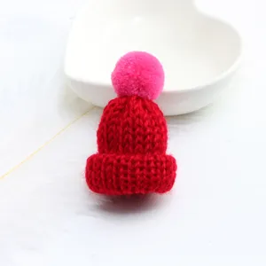 Close-up detail of cute miniature red knitted pom-pom hat accessory for bags and crafts.