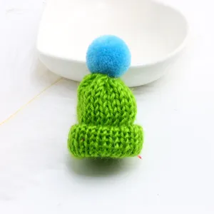 Mini knitted hat detail shot, showing green yarn texture and cute blue pom-pom decoration.