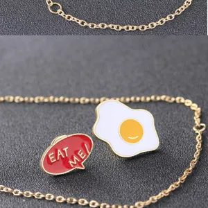 Nahaufnahme des süßen Spiegelei und EAT ME Sprechblasen Emaille Pin Sets mit goldener Kette.