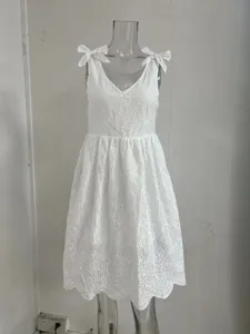 Détail de robe blanche sans manches en dentelle brodée à col V et nœuds sur les épaules.