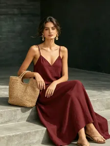 Detail shot of a women's solid burgundy spaghetti strap maxi dress paired with a woven straw bag.