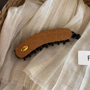 Detailed shot of the woven banana hair clip featuring a gold metal accent and secure teeth.