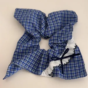 Detailed view of blue plaid hair scrunchie featuring cute lace ruffle and navy bow accent.