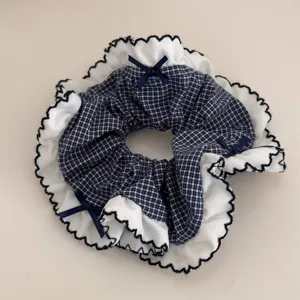 Navy blue plaid hair scrunchie with white lace ruffle trim and cute bows. Detail view for hair.