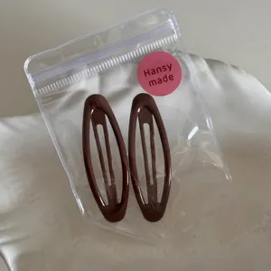 Nahaufnahme brauner ovaler Haarklammern in transparenter Verpackung, minimalistisches Haar-Accessoire.