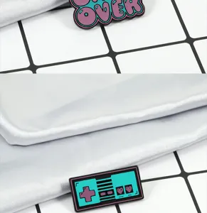 Primer plano detallado del broche esmaltado de juego retro con diseño game over y mando.