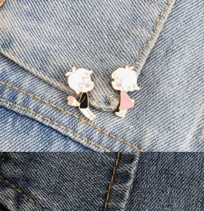 Cute cartoon couple enamel pins close up detail showing sweet boy and girl on denim fabric.