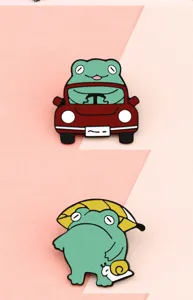 Close-up detail of cute green frog enamel brooch pins, featuring car driving and snail styles.