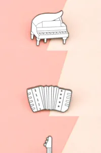 Detailed close-up of white musical instrument enamel pin set featuring piano and accordion.