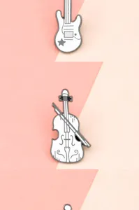 Close-up detail shot of white musical instrument enamel pins, guitar and violin metal badges.