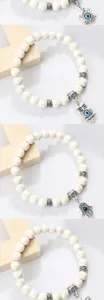 Vue détaillée du bracelet de perles blanches avec des pendentifs œil et des intercalaires en métal.