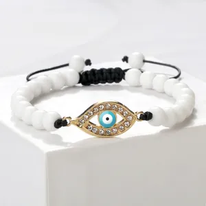 Bracelet de perles œil maléfique blanc avec pendentif strass doré et cordon noir réglable.