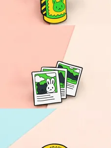 Enamel pin detail shot showing cute camera and polaroid photo design with cartoon elements.