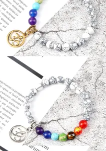 Detail van de chakra kralenarmband met kleurrijke stenen, witte howliet en metalen Om-hangertje.