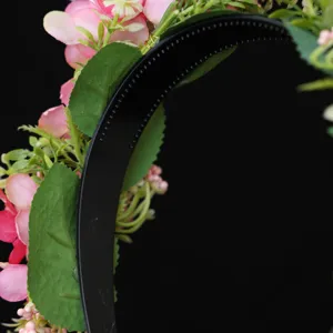 Close up view of the black plastic headband decorated with pink floral and green leaves.