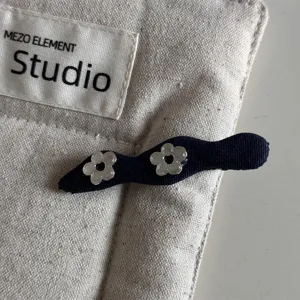 Close-up of a dark blue fabric hair clip with cute silver flower decorations on a canvas.